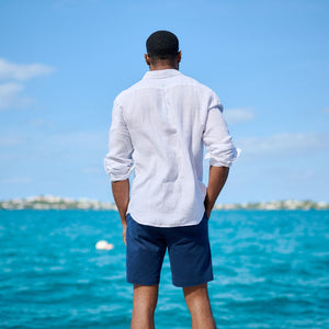 Man standing on a dock facing the ocean with a clear blue sky.