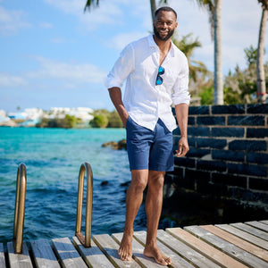 Man standing on a wooden dock by the water with palm trees in the background
