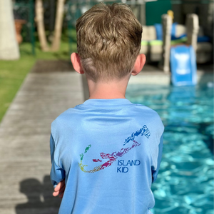 Child wearing a blue 'Island Kid' shirt by a pool