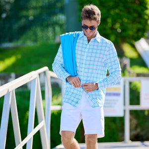 Man walking on a wooden dock wearing a light blue checkered shirt and white shorts.