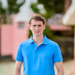 Man wearing a blue polo shirt and light pink pants standing outdoors.
