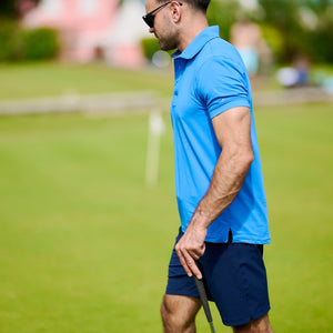 Man in blue polo shirt and shorts holding a golf club on a golf course