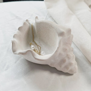 White ceramic shell-shaped jewelry dish with a necklace on a white surface.