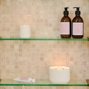 Glass shelves in a tiled bathroom with various bottles and candles.