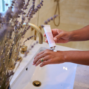 Person washing hands with soap in a bathroom setting with lavender plants.