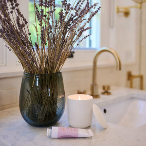 Vase with lavender on a bathroom counter next to a candle and soap.