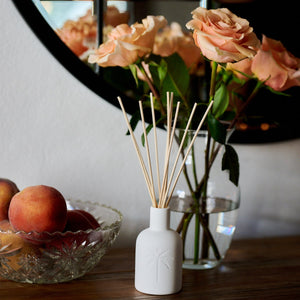 White diffuser bottle on a table with peach slices and flowers in the background