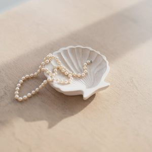 Pearl necklace draped over a white shell on a light wooden surface