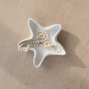 Star-shaped white dish with a gold necklace on a beige surface