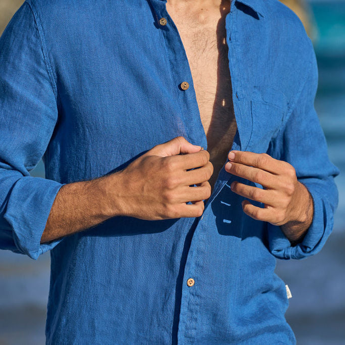 Man in a blue shirt unbuttoning his shirt with a blurred beach background