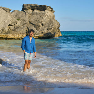 Man standing on a beach with rocky outcrop and clear blue water