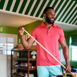 Man in a pink shirt holding a pool cue next to a pool table with colorful balls.