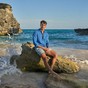 Man sitting on a rock by the ocean with cliffs in the background