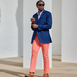 Man in a blue blazer and pink pants standing against a white wall.