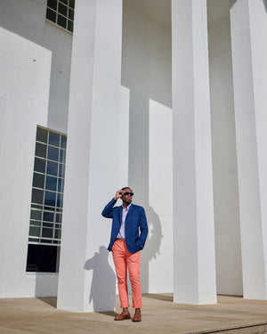 Man in a blue jacket and pink pants standing in front of a white building with columns.