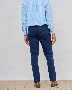 Man wearing a blue checkered shirt and navy pants against a white wall.