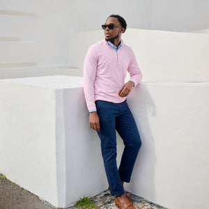 Man in pink sweater and blue pants leaning against a white wall.