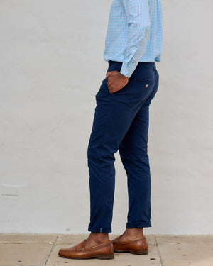 Person wearing a light blue checkered shirt, navy pants, and brown shoes against a plain background
