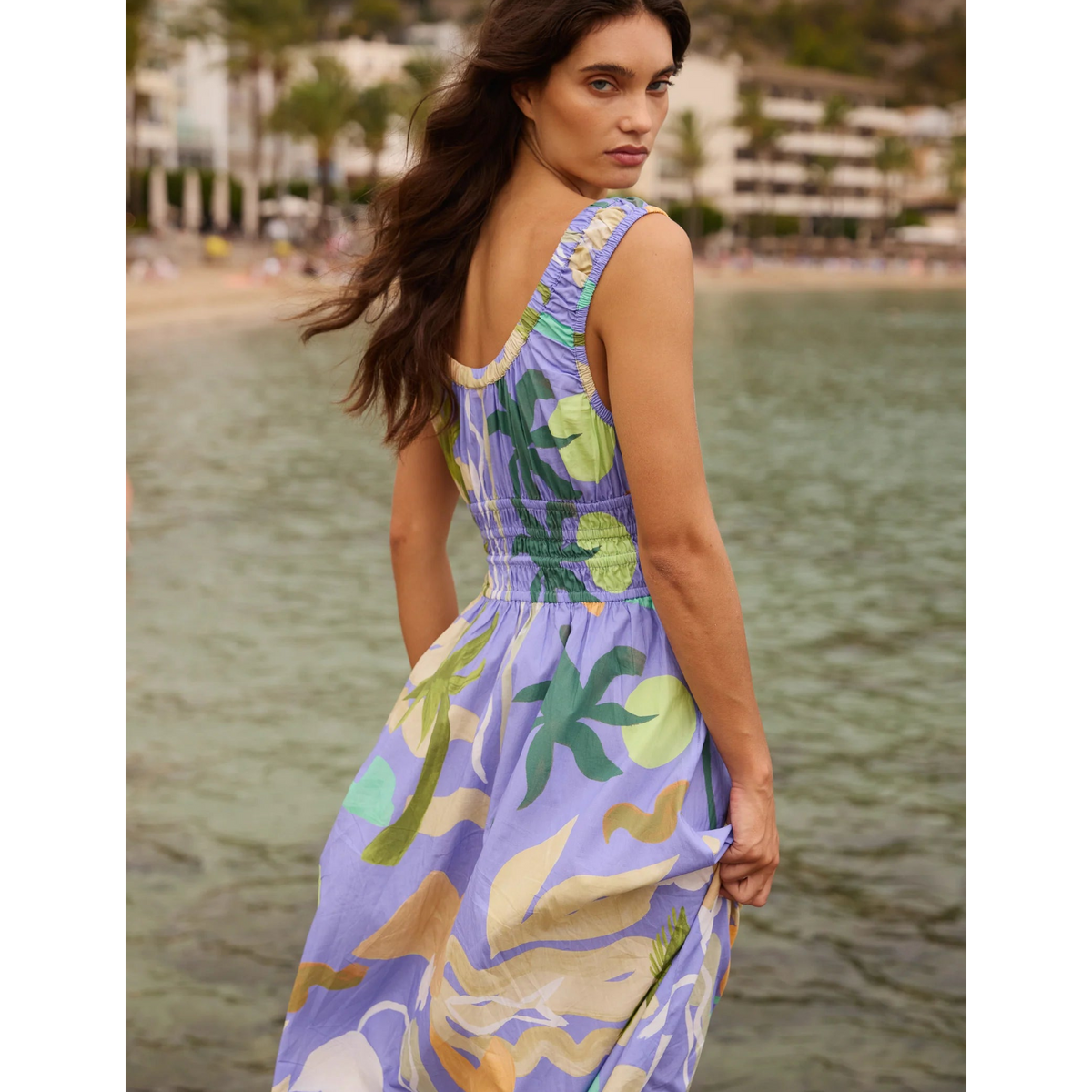 Woman in a colorful dress standing by a body of water with a scenic background.