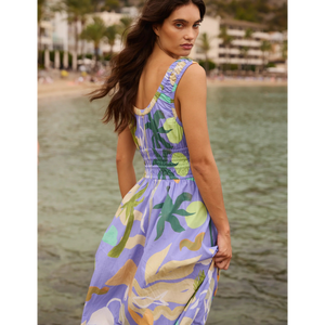 Woman in a colorful dress standing by a body of water with a scenic background.