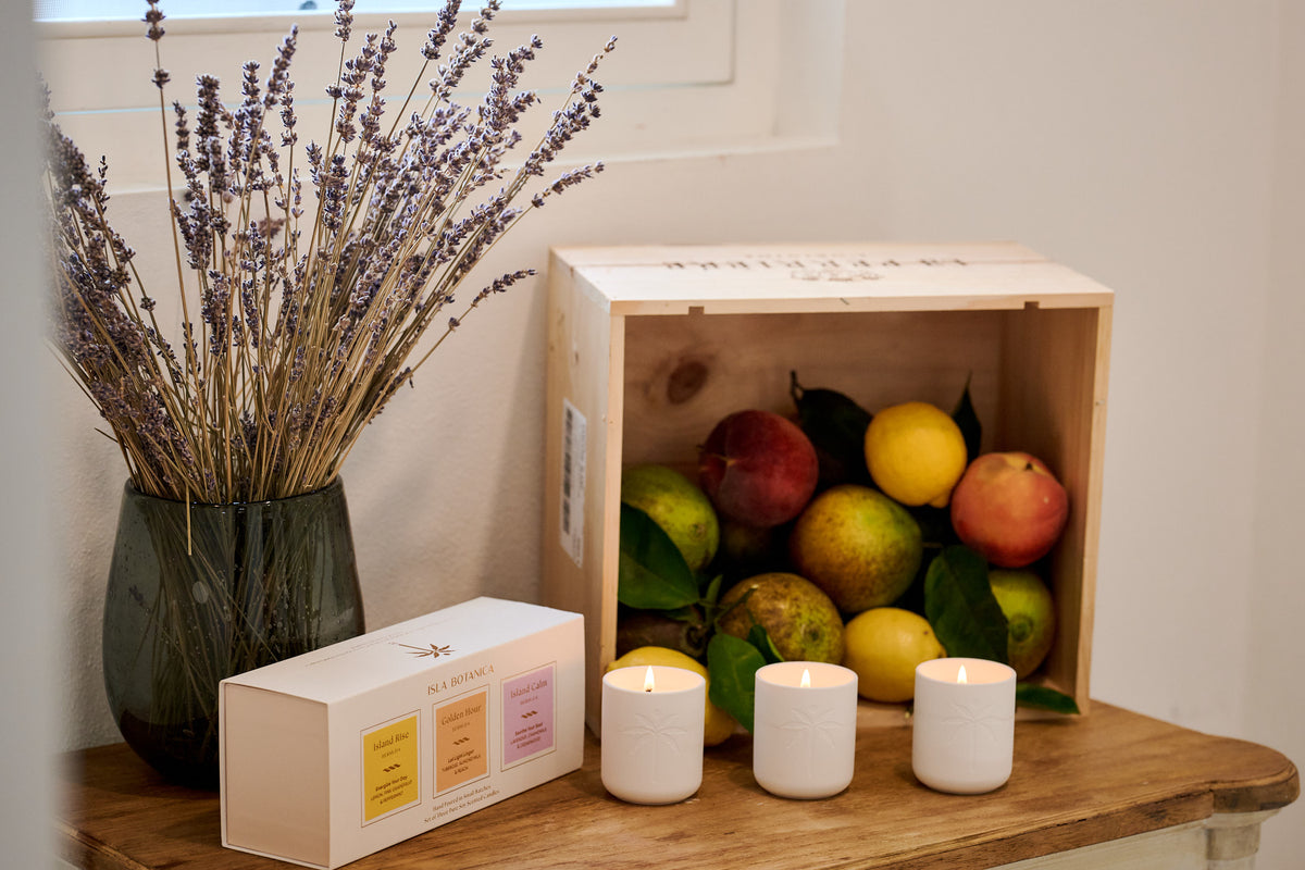 Wooden crate with fruits, candles, and a vase of lavender on a wooden surface.