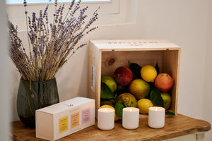 Wooden crate with fruits, candles, and a vase of lavender on a wooden surface.
