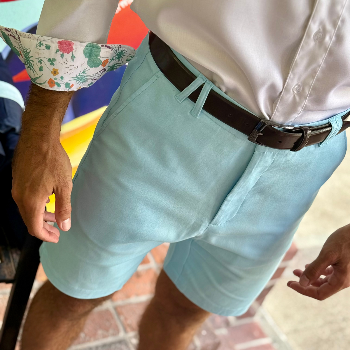 Person wearing light blue shorts with a colorful shirt cuff on a brick pavement.