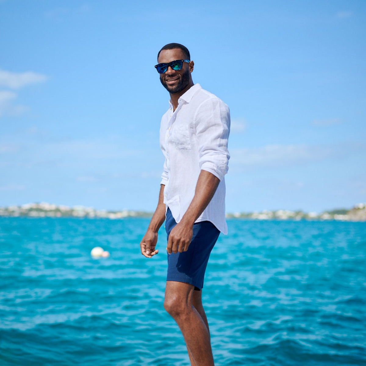 Man standing on a dock by the ocean wearing sunglasses and a white shirt.