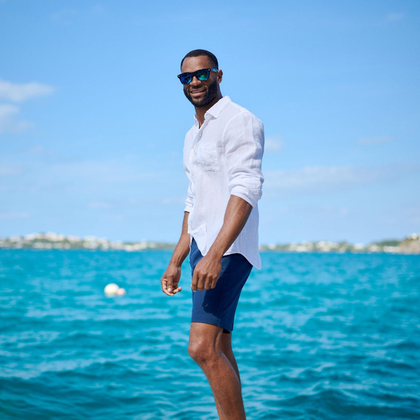 Man standing on a dock by the ocean wearing sunglasses and a white shirt.