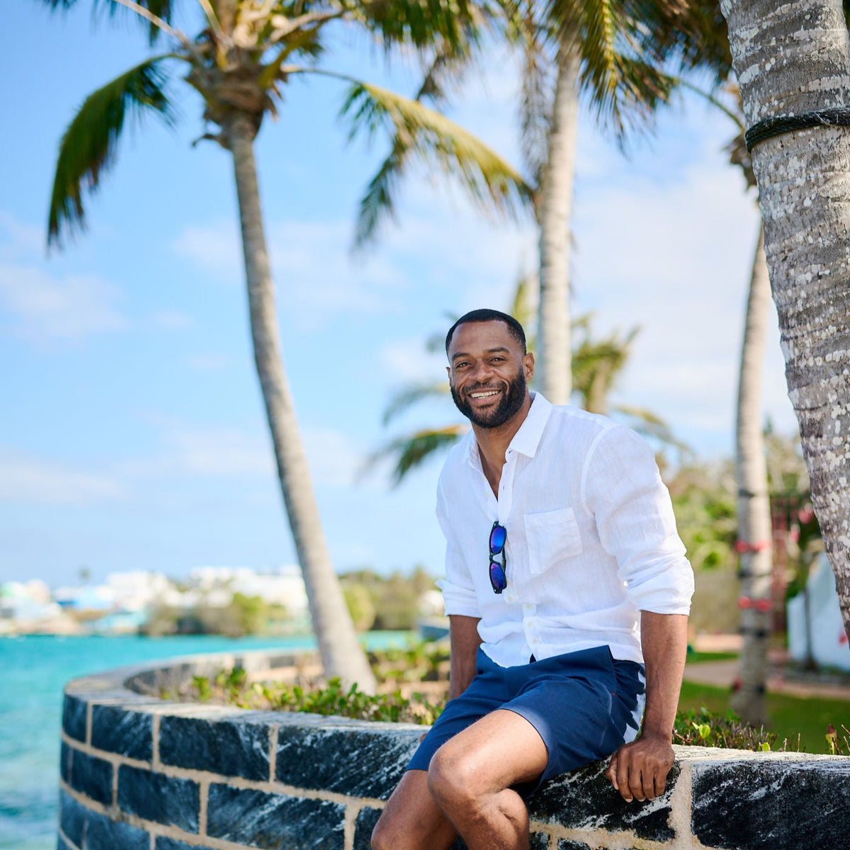 Man sitting on a stone wall with palm trees and ocean in the background
