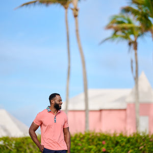 Man standing on a golf course with palm trees and a pink building in the background