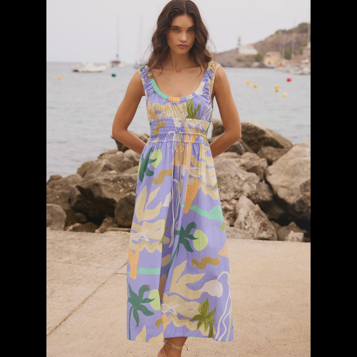 Woman wearing a colorful dress standing by a waterfront with rocks and water in the background