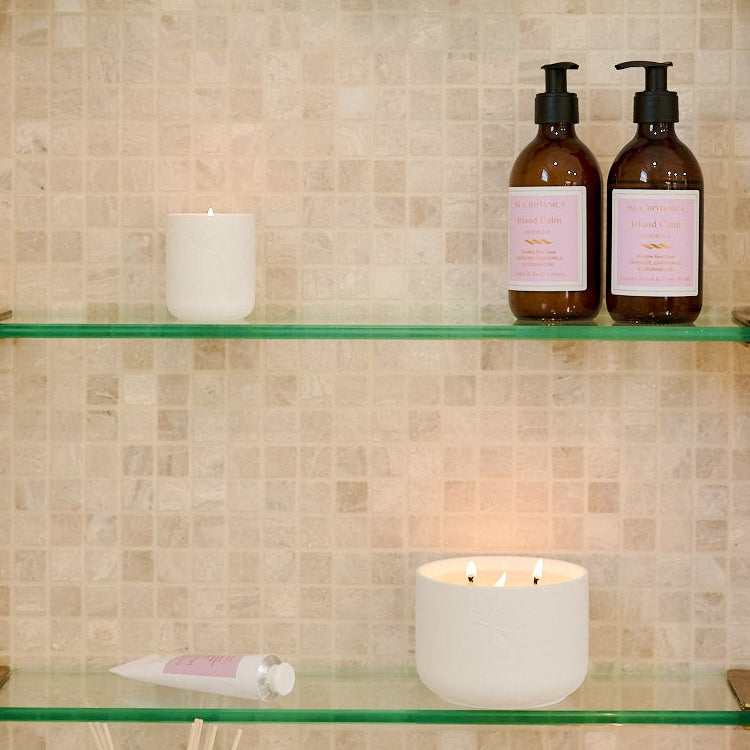 Glass shelves in a tiled bathroom with various bottles and candles.