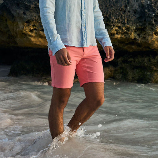 Man standing in shallow water near rocky cliffs on a sunny day