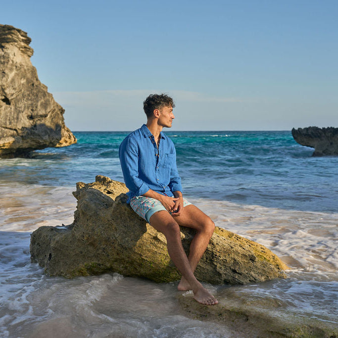 Person sitting on a rock by the ocean with cliffs in the background