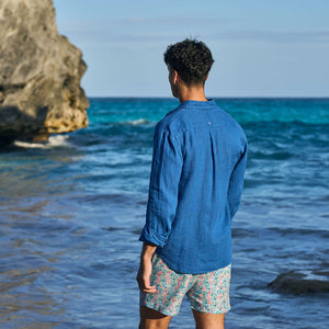 Man standing on a beach looking at the ocean with a rock formation in the background