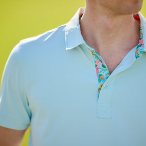 Light blue polo shirt with floral collar against a blurred green background