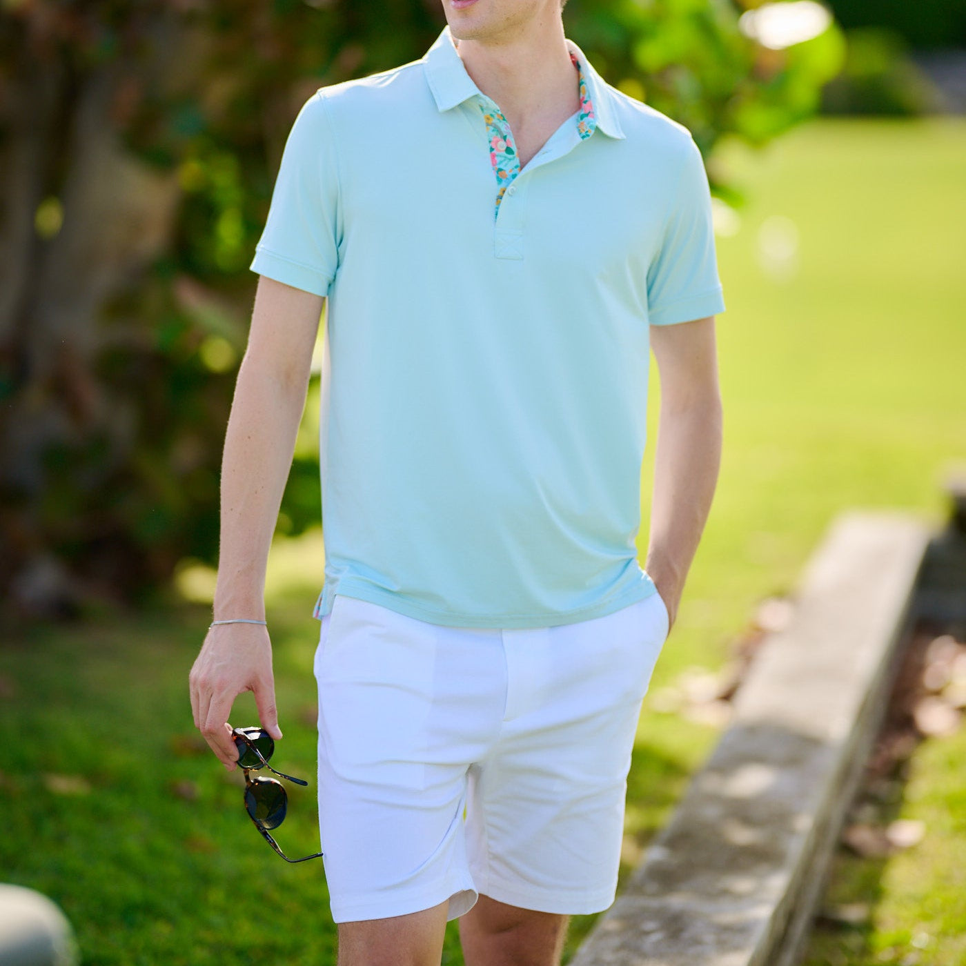 Light blue polo shirt with floral collar against a blurred green background