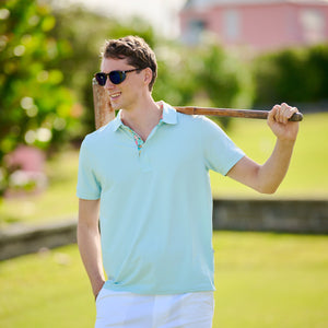 Man in light blue polo shirt and white shorts holding a golf club on a grassy field.