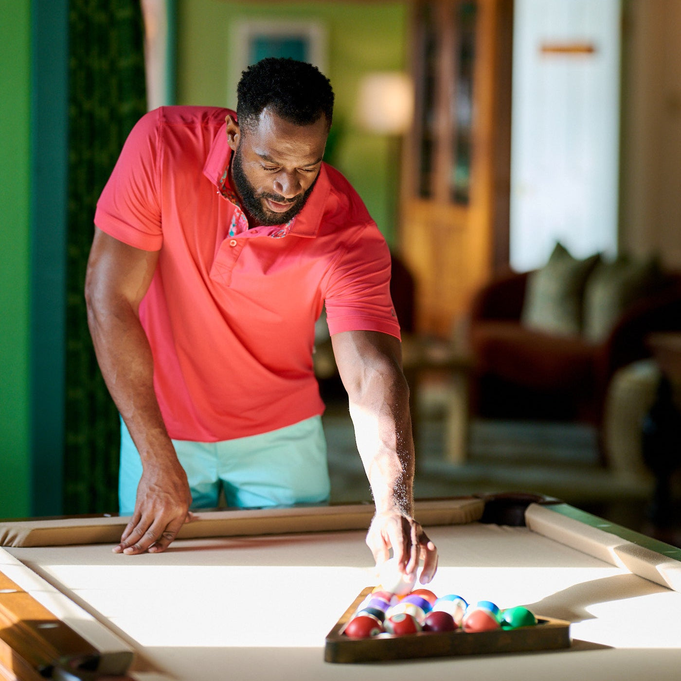 Man in a pink shirt holding a pool cue indoors
