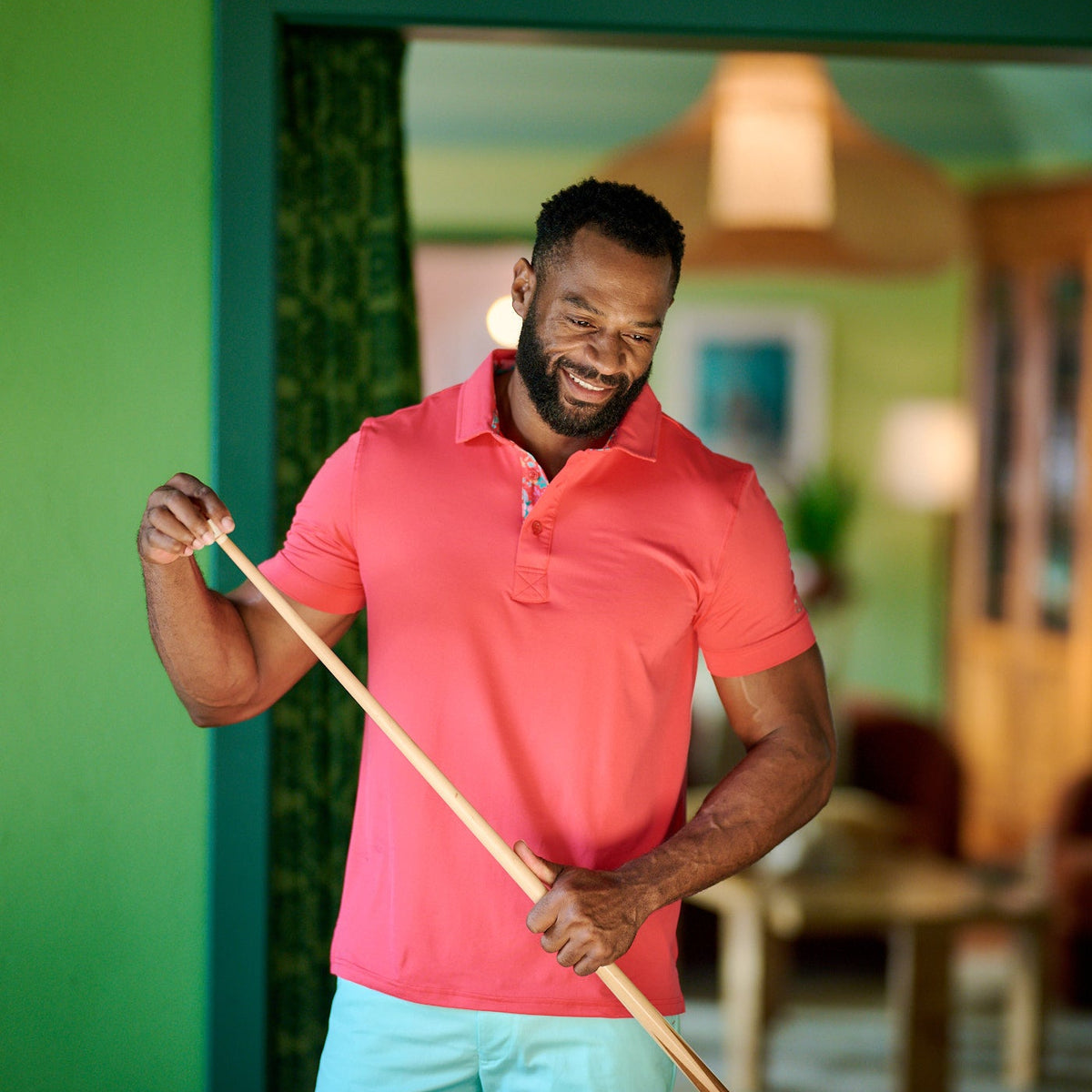 Man in a pink shirt holding a pool cue indoors