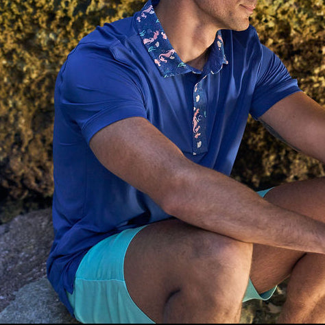 Man in a blue shirt and light green shorts sitting against a rocky background