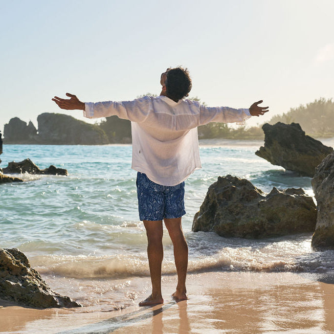 Man standing on a beach with arms outstretched, facing the ocean.