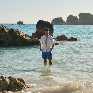 Man standing in shallow water near rocks on a beach
