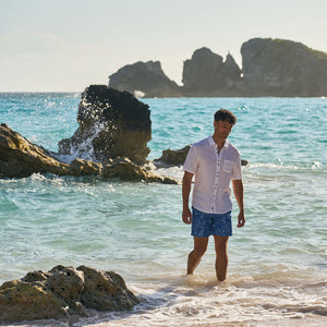 Man walking in shallow water near rocks on a beach