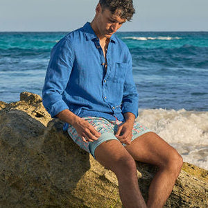 Man sitting on a rock by the ocean with clear blue water and cliffs in the background