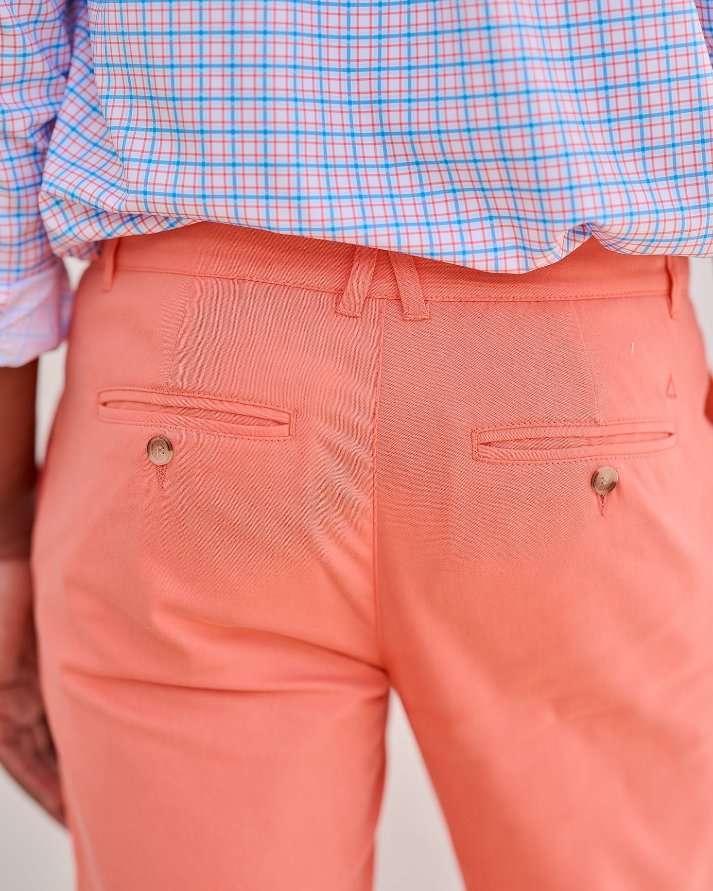 Person wearing a checkered shirt and coral pants on a beige background