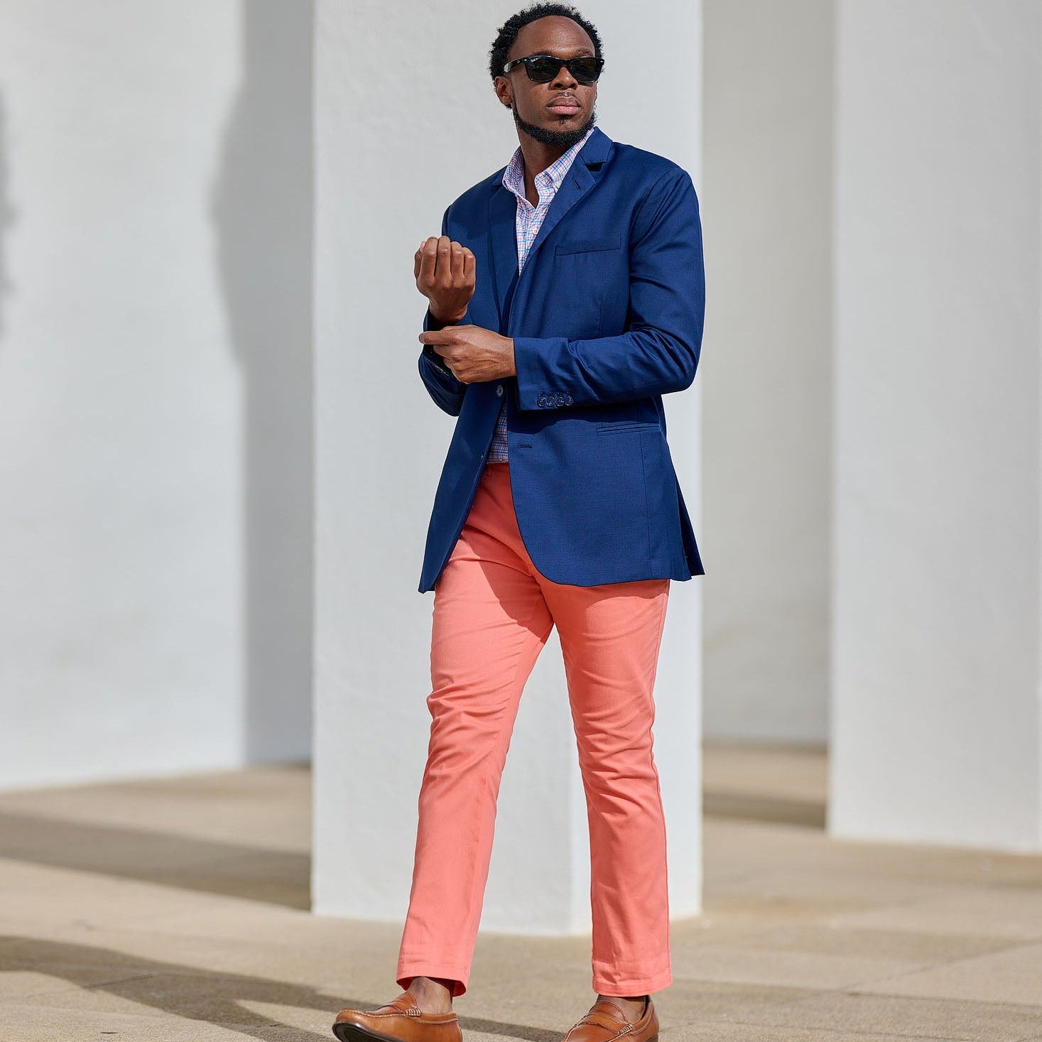 Man in a blue blazer and pink pants standing against a white wall.
