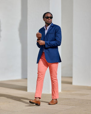 Man in a blue blazer and pink pants standing against a white wall.