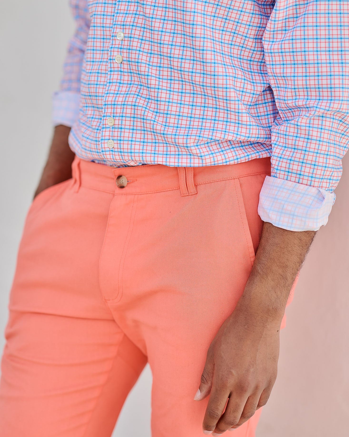 Person wearing a checkered shirt and coral pants against a neutral background